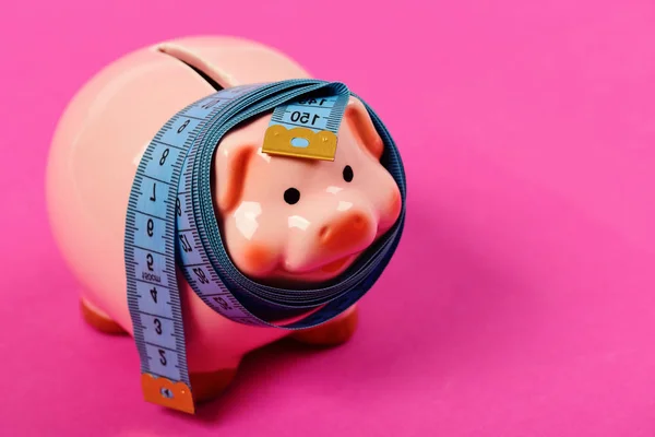 Piggy bank tied with measuring tape. Budget and squeezed savings — Stock Photo, Image