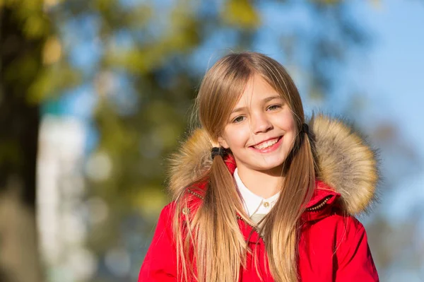 Buen humor en el clima de otoño. Niña usar abrigo para la temporada de otoño. Niño alegre caminando vistiendo abrigo cálido brillante o chaqueta caída día soleado. Chica sonriente cara capa de otoño de moda con capucha y piel — Foto de Stock