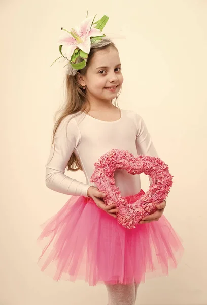 Malá šťastná dívka s lily ve vlasech drží růžové srdce — Stock fotografie