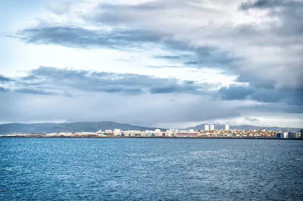 Πόλη στη θαλάσσια ακτή της Ισλανδίας. Σκανδιναβική έννοια θαλασσογραφία. Ηρεμία επιφάνεια του νερού και της πόλης με ψηλά κτίρια σύγχρονης αρχιτεκτονικής. Σκανδιναβική πόλη στην ακτή. Ρέικιαβικ θαλασσογραφία δραματικός συννεφιασμένος ουρανός — Φωτογραφία Αρχείου