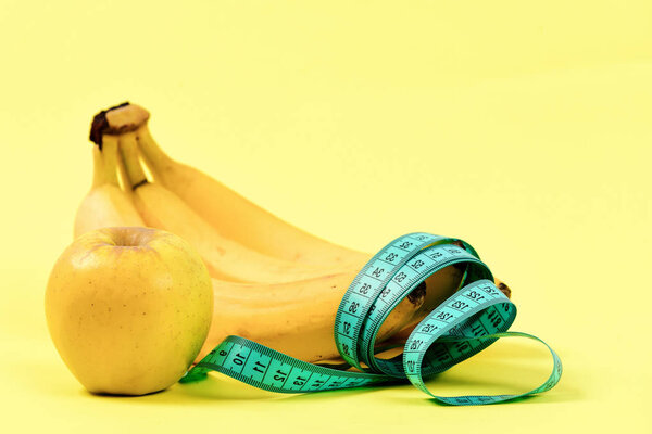 Tape for measuring, bunch of bananas and ripe apple,