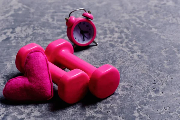 Hantlar i rosa färg bredvid väckarklocka och hjärta — Stockfoto