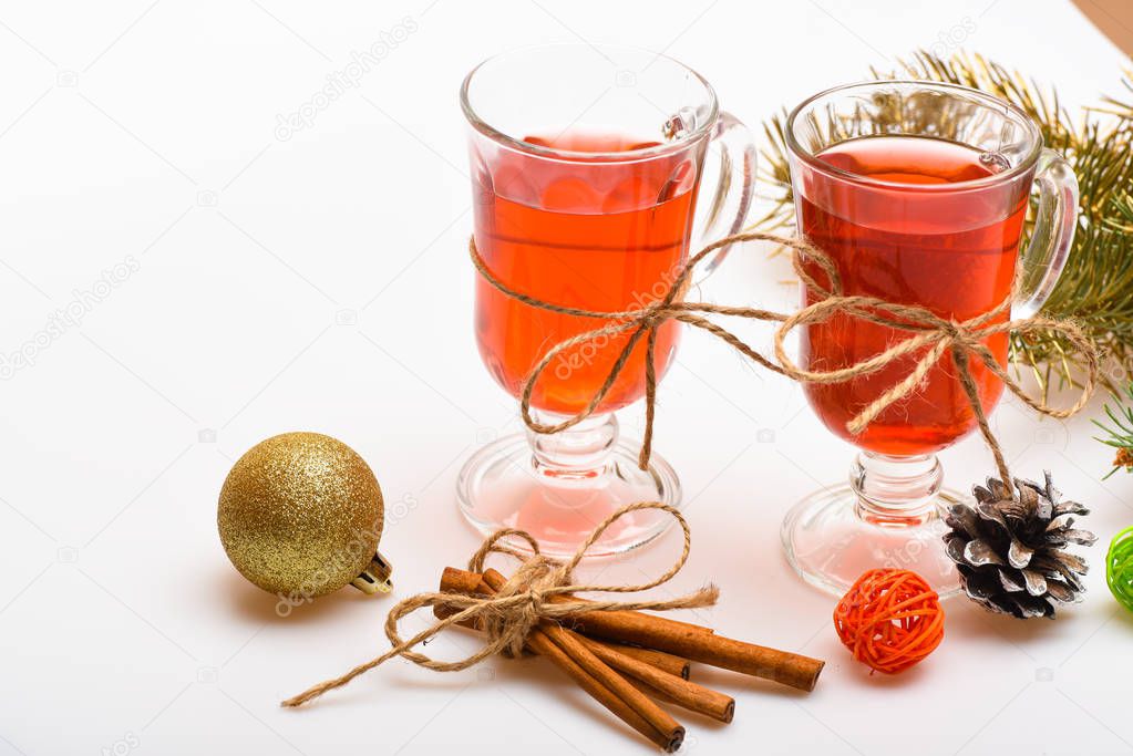 Traditional mulled wine with spices near fir branch. Mulled wine or hot beverage and cinnamon sticks. Winter drink concept. Glass cup of delicious mulled wine with Christmas decor on white background