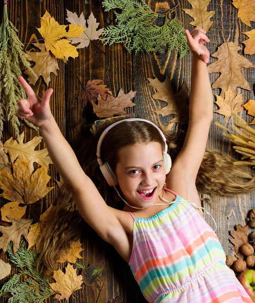 Happy childhood. Kid girl wooden background listen music headphones. Child listen music relaxing top view. Autumn melody concept. Autumn music playlist. Best songs about fall. Enjoy music and relax