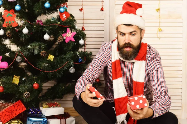 Guy in hat and scarf sits by Christmas tree — Stock Photo, Image