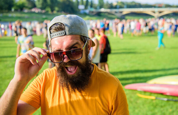 Человек смотрит через солнечные очки солнечный день на открытом воздухе. Празднование городского события. Хипстер в кепке посещает фестиваль пикников. Человек бородатый хипстер перед толпой людей зеленый фон поля
