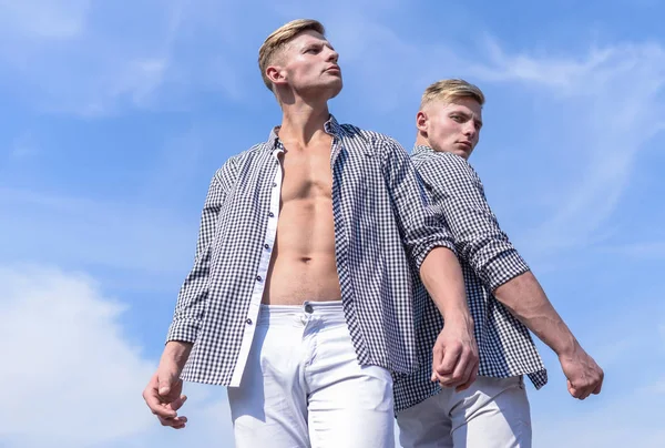 Men strong athlete wear same shirts. Menswear and fashion concept. Brothers twins looks attractive. Fashionable similar outfits. Men twins brothers muscular guys posing in shirts sky background.