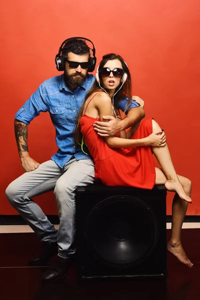 Couple in love sits on black loudspeaker on red background