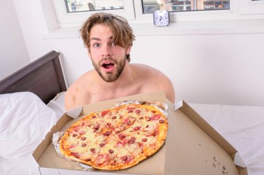 Adam yakışıklı adam yatakta kahvaltı için peynirli yemek yeme sakallı. Adam pizza kutusu sit yatak yatak odası ya da otel odasında tutar. Gıda teslim Servisi. Adam, kahvaltıda pizza seviyor. Diyet hakkında kimin umurunda