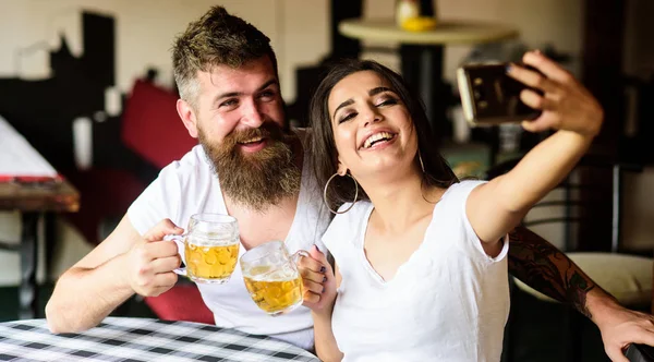 Couple cheerful mood drinking beer in pub. Take selfie photo to remember great date in pub. Man bearded hipster and girl with beer glass full of craft beer. Couple in love on date drinks beer