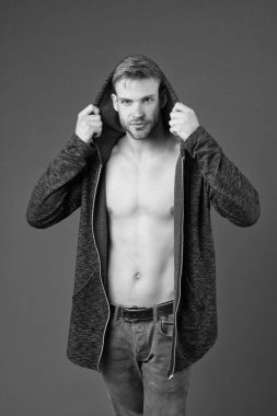 Gülen suratlı adam kapüşonlu, mor arka planlı ceketi deniyor. Yüzünde kıllar, göğsünde pürüzsüz bir deri olan adam giyinmeye çalışıyor. Moda konsepti. Adam uzun kapüşonlu ceketle çekici görünüyor.