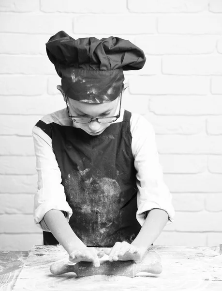 若い男の子かわいい料理人赤の制服と帽子ステンドグラスがテーブルの近くに立っている粉ロールピンを保持し、白いレンガの壁の背景に料理 — ストック写真