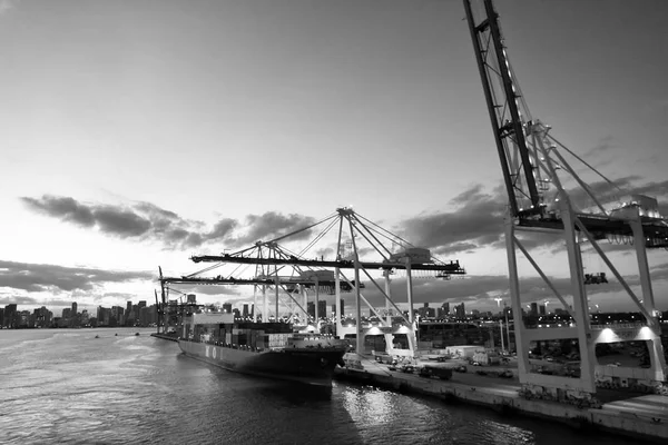 Navio de carga e guindastes no porto marítimo no céu noturno. Porto ou terminal marítimo de contentores. Transporte de mercadorias e mercadorias. Conceito de transporte e transporte de água — Fotografia de Stock