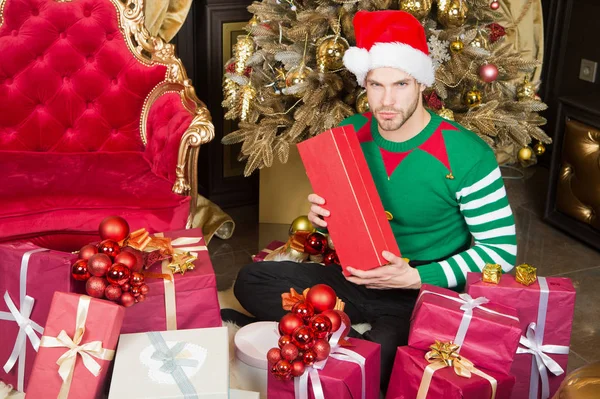 Чоловік Санта-капелюх відзначає різдвяний бароковий інтер'єр, прикрашений ялинкою та подарунками. Традиції святкування Різдва. Чоловік святкує Новий рік або Різдво. Санта-Клаус і концепція різдвяних подарунків — стокове фото
