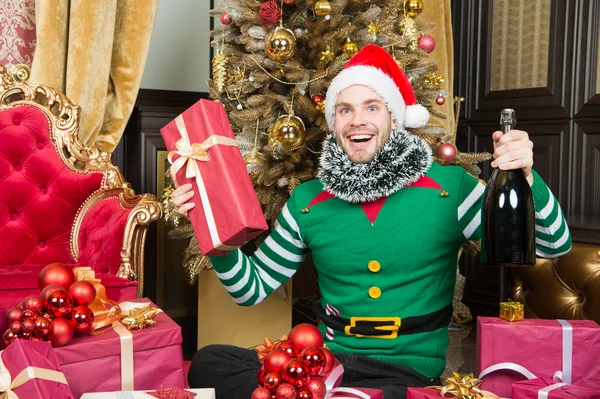 Санта и рождественские подарки концепция. Мужчина носит одежду эльфа санты и празднует рождественский интерьер украшенной елкой и подарками. Рождественское шампанское. Человек празднует Новый год или Рождество — стоковое фото