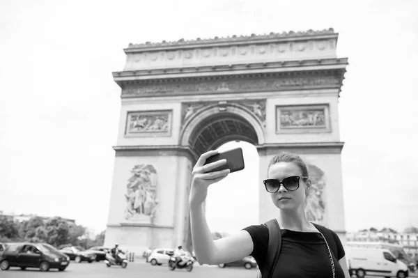 Mulher com smartphone no arco monumento em Paris, França. Mulher fazer selfie com telefone no arco de triomphe. Férias e passeios na capital francesa. Menina com aparência de moda e beleza sensual — Fotografia de Stock