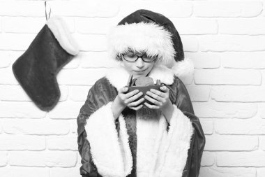 Dekoratif Noel ile kırmızı kazak ve yeni yıl şapkalı Genç Sevimli Noel baba çocuk ile gözlük veya çorap xmas veya önyükleme tutun ve kase beyaz tuğla duvar zemin üzerine çikolata kalça kurabiye burnunu çekmek