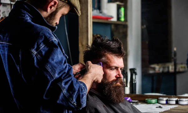 Barbeiro com clipper aparar o cabelo no templo do cliente. Um cliente Hipster a cortar o cabelo. Conceito de estilo de vida Hipster. Barbeiro com cortador de cabelo funciona no penteado para barbearia homem barbudo fundo — Fotografia de Stock