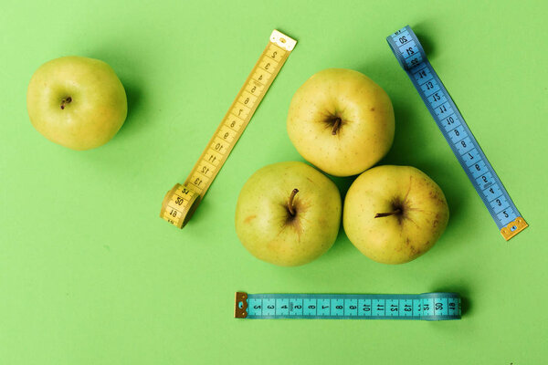 Apples near measuring tape rolls on green background, top view