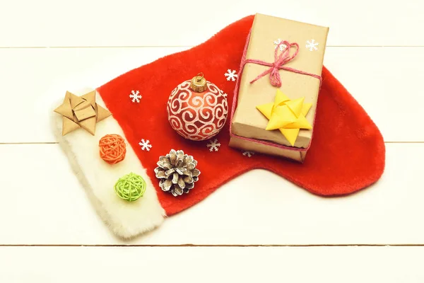 Colorful Christmas or New Year decoration include gift with rose string, yellow bow, Santa Claus red sock, red ball, brown bow, pine cone, colorful clews and snowflakes on vintage wooden background. — Stock Photo, Image