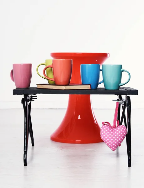 Красный стул и черный деревянный поднос с красочными чашками и книгу на нем пот розовое сердце на белом фоне — стоковое фото