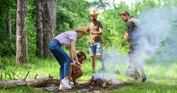 Company friends or family making bonfire in forest nature background. Friends working as team to keep bonfire. Company camping forest prepare bonfire for picnic. Add some wood to fire