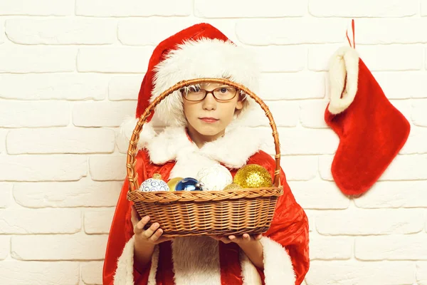 年轻可爱的圣诞老人男孩戴着眼镜在红色的毛衣和新年帽子持有用五颜六色的气球与放养或引导上白砖的背景墙上的装饰圣诞节或圣诞斗 — 图库照片