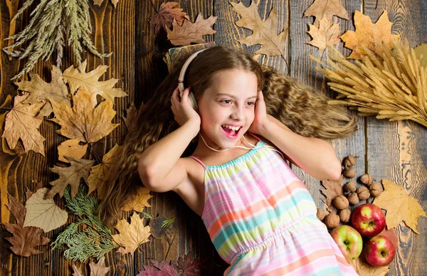 Kid listen music headphones wooden background. Child listen music relaxing top view. Fall melody concept. Fall music playlist. Best songs about fall. Enjoy music and relax. Girl lay fallen leaves