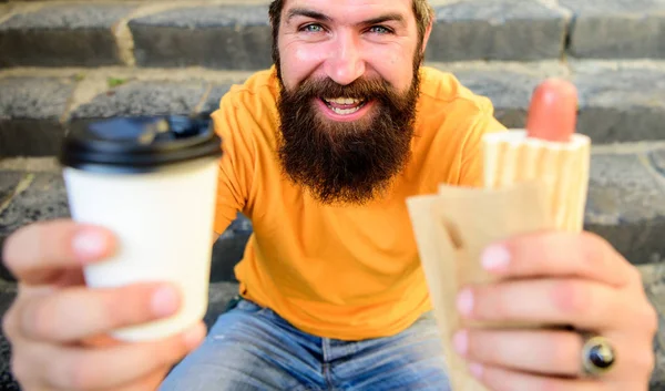 Fast food para almoço ideia comum. Hipster desfrutar de cachorro-quente e beber bebida copo de papel. Homem barbudo desfrutar rua comida escadas fundo. Hipster come cachorro-quente e bebe café. Conceito de hora de almoço — Fotografia de Stock