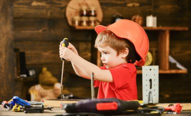 Handcrafting ve atölye kavramı. Yürümeye başlayan çocuk meşgul yüzündeki tornavida ile Atölyesi'nde oynamaktadır. Çocuk Çocuk Tornavida Aracı tutar. Kask Oluşturucu veya repairer, veya handcrafting şirin çocuk