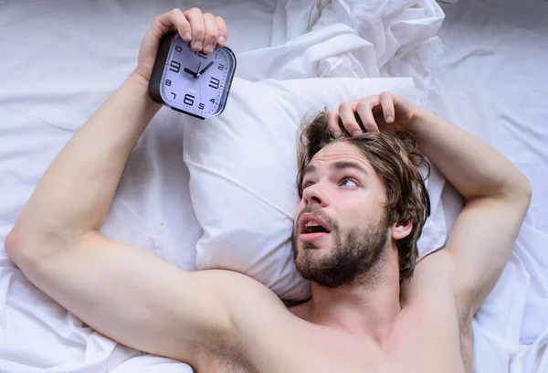 Get up early morning tips. Oversleep problem. Toughest part of morning simply getting out of bed. Man unshaven surprised shocked face lay pillow alarm clock top view. Guy missed alarm clock ringing