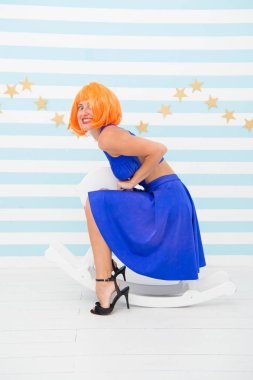 Lady Red ya da kızıl peruk mavi elbise sallanan ata biner. Komik ve komik bir kavram. Neşeli kadın eğleniyor. Eğlence ve eğlence. Kız peruğu sallanan küçük bir at. Çocuksu hissediyorum.
