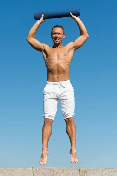 Tot gezonde levensstijl. Man met yoga mat gevangen in medio lucht hemelachtergrond. Sportman met mat sprong. Opleiding buiten. Het rekken van spieren na training. Yoga-lessen. Praktijk yoga of strekken — Stockfoto