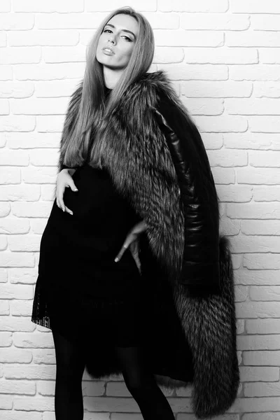 Μοντέρνα σέξι όμορφη γυναίκα ή κορίτσι με όμορφα μακριά ξανθά μαλλιά στην μέση παλτό της Βουργουνδίας γούνας με μαύρα δερμάτινα μανίκια φόρεμα και τη μόδα μακιγιάζ σε λευκό τούβλο τοίχο studio φόντο — Φωτογραφία Αρχείου