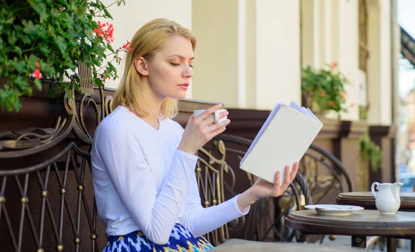Дівчина п'є каву, читаючи нову книгу бестселерів популярного автора. Ідеальна концепція ранку. Найкраще поєднання кави та цікавої книги ідеальні вихідні. Жінка п'є терасу кафе на відкритому повітрі — стокове фото
