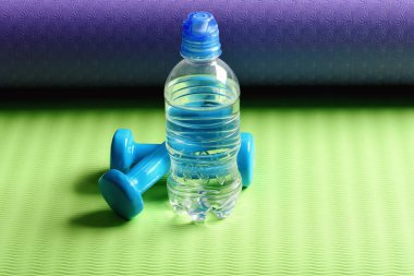 Yoga minderindeki plastik halterlerin yanında su var. Spor ve sağlık