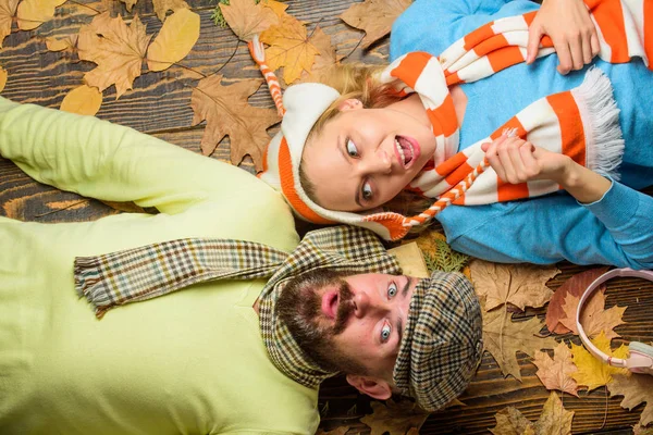Fall date pleasant cozy atmosphere. Autumn date concept. Man bearded cheerful face and lady lay on wooden background with leaves top view. Couple in love wear hats scarves enjoy autumn cozy season
