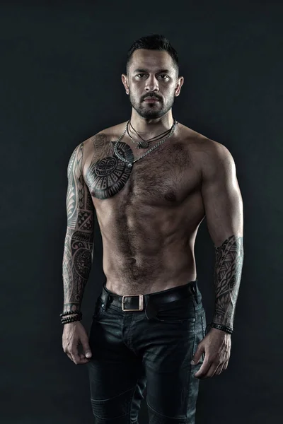 Arte del tatuaggio. Bell'uomo in posa in jeans con tatuaggio. Uomo bello senza maglietta muscolare con jeans su sfondo scuro. Atleta tatuato muscolare aspetto attraente. Concetto sport e moda — Foto Stock