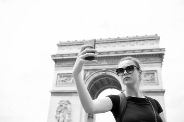 Paris, Fransa 'daki Arc de Triomphe' de bir kadın telefonla selfie çekiyor. Kemer Anıtı 'nda akıllı telefonu olan bir kadın. Fransa 'nın başkentinde tatil ve gezi. Moda görünümlü ve şehvetli bir kız.