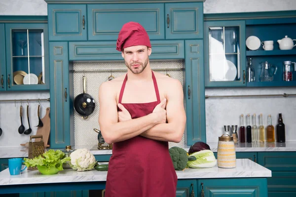 Hombre atractivo desnudo chef usar delantal y sombrero. Sexy chef muscular en frente de la cocina. Atractivo chef listo para cocinar. Chef musculoso posando en la cocina. Cocinar deliciosa receta. Sexy macho cocina comida — Foto de Stock