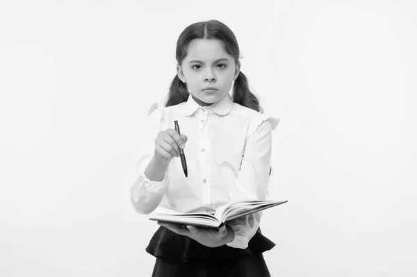 Girl cute serious face yellow background. Child girl school uniform clothes holds book and pen. Check my homework. Child school uniform smart kid done with homework. Check knowledge concept — Stock Photo, Image