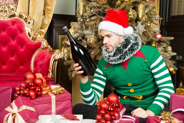 O homem celebra o Ano Novo ou as férias de Natal. Papai Noel e presentes de Natal conceito. Homem usar roupas de elfo santa chapéu celebrar Natal interior decorado abeto e presentes. Bebida de champanhe de Natal — Fotografia de Stock