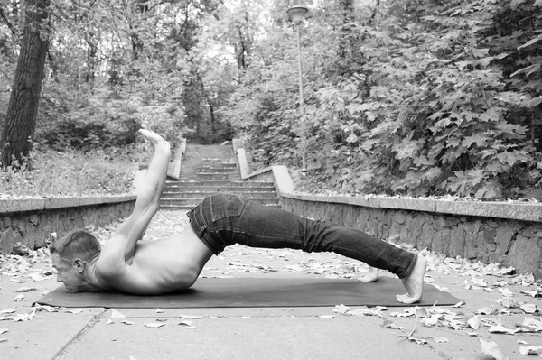 Man beoefenen van yoga buiten in park, natuur op achtergrond. Man met naakt romp het beoefenen van asana op yoga mat. Gezonde levensstijl concept. Sportman begint zijn dag met yoga oefeningen in park — Stockfoto