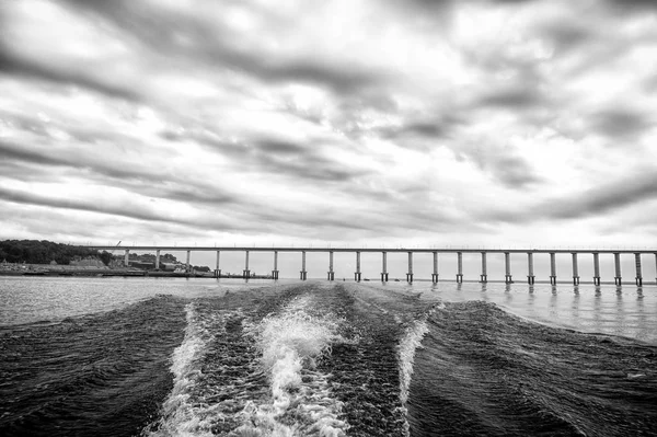 Spuren von Schnellbooten auf blauem Meerwasser in Manaus, Brasilien. Meereslandschaft mit Brücke am Horizont am bewölkten Himmel. Reisen und Urlaub. Architektur und Designkonzept — Stockfoto