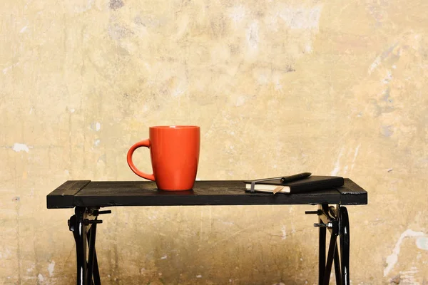 Ζεστό ρόφημα και blogging έννοια. Τετράδιο με σελιδοδείκτη, στυλό και κόκκινο Κύπελλο σε τραπέζι κοντά σε τοίχο. Ημερολόγιο με στυλό και νέα φλιτζάνι πρωί ποτό σε εσωτερικούς χώρους. Τσάι ή καφές στον μαύρο πίνακα σε μοντέρνο εσωτερικό — Φωτογραφία Αρχείου