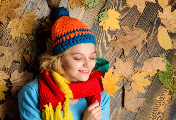 Pleasant moments. Fall cozy atmosphere. Girl cheerful face lay on wooden background with orange leaves top view. Fall and autumn season concept. Hipster woman knitted hat and scarf hold autumn leaves