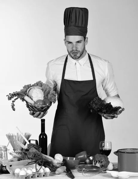 Chef with tired face holds baskets with lettuce and cabbage