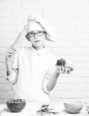 Beyaz üniformalı, şapkalı, çikolatalı kekleri olan ve masasının yanında renkli kaseleri olan yuvarlak raptiyeli yakışıklı aşçı şefi.