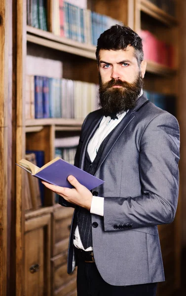 Confianza, éxito, educación, investigación, concepto de literatura. El profesor tiene un libro en la biblioteca vintage. El hombre barbudo con traje inteligente está cerca de la librería. Hombre maduro con cara confiada y barba larga — Foto de Stock