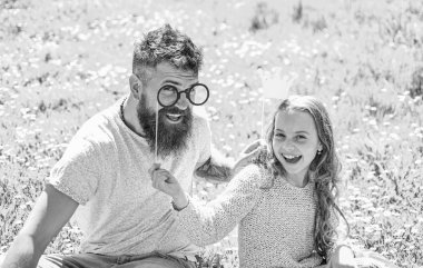 Baba ve kızı, grassplot, arka planı yeşil çimenlerin üzerinde oturur. Daddys Prenses kavramı. Çocuk ve babası crown ve gözlük ile poz booth öznitelikleri fotoğraf. Aile harcamak açık havada eğlence